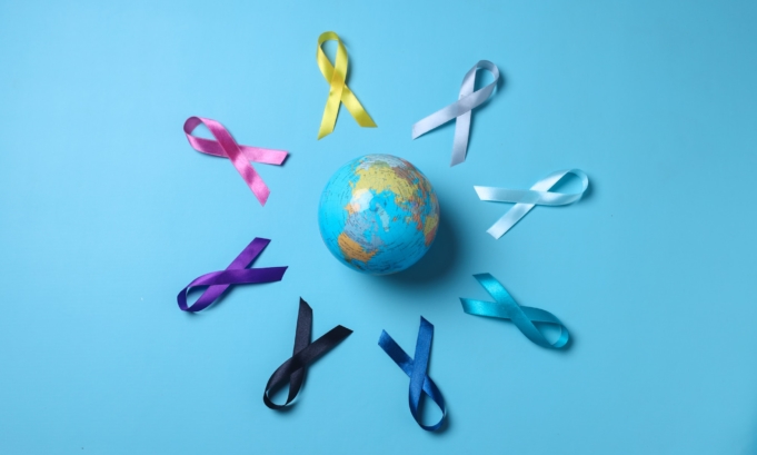 Earth globe surrounded by colorful awareness ribbons on blue background. World cancer day concept.