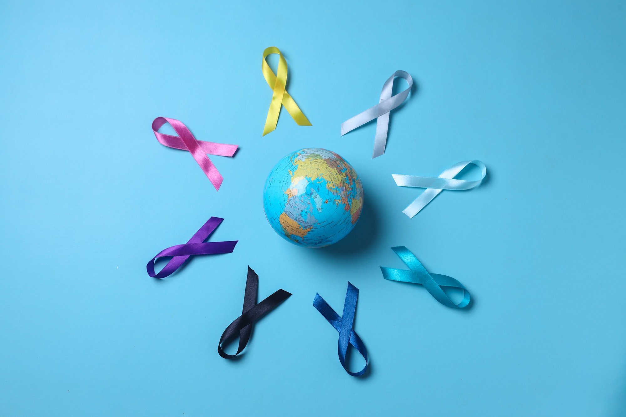 Earth globe surrounded by colorful awareness ribbons on blue background. World cancer day concept.