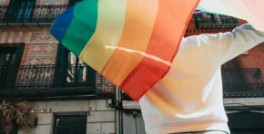 Young man holding a pride lgtbi rainbow flag on his back while walking on the streets