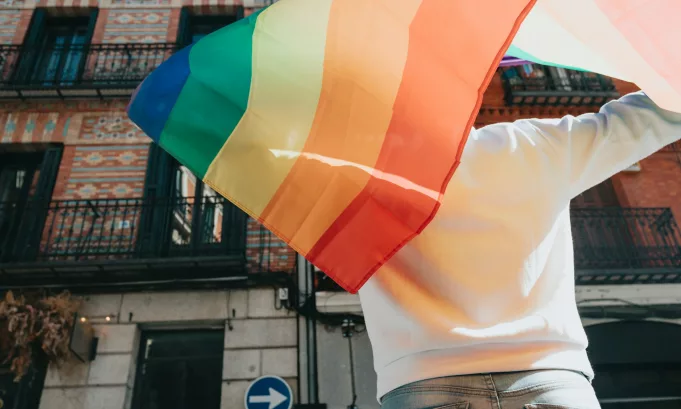 Young man holding a pride lgtbi rainbow flag on his back while walking on the streets