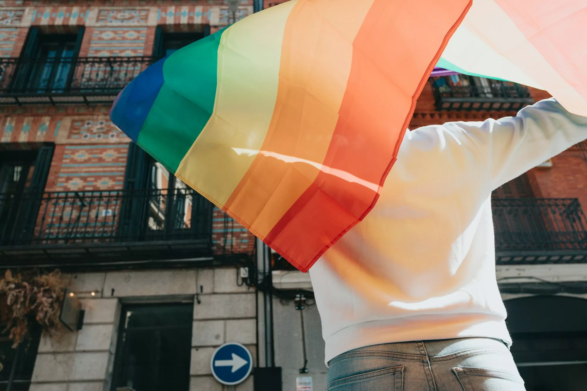 Young man holding a pride lgtbi rainbow flag on his back while walking on the streets