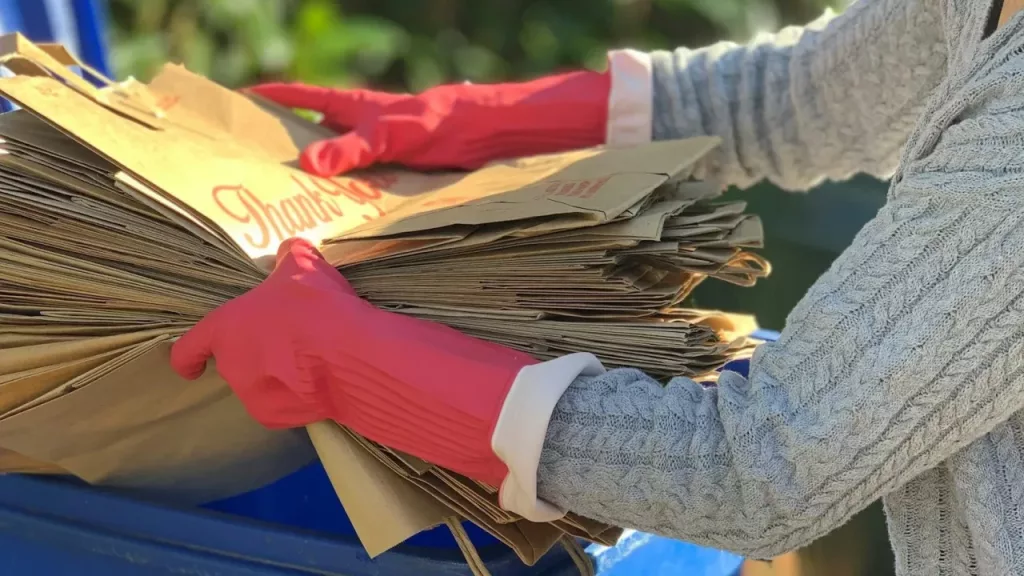 Woman on her daily chore, recycling paper bags on recycling bin to help our environment. Ecofriendly